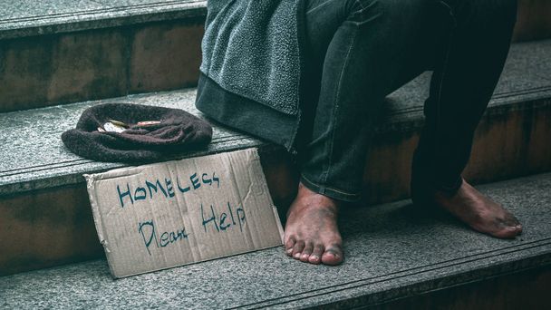 Close-up van voeten van arme dakloze man of vluchteling zittend op de trap van stedelijke straat van de stad bedelen voor geld. - Foto, afbeelding