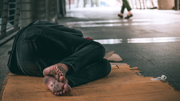 Cerca de los pies de pobre hombre sin hogar o refugiado durmiendo en el piso sucio en la calle urbana de la ciudad
. - Foto, Imagen