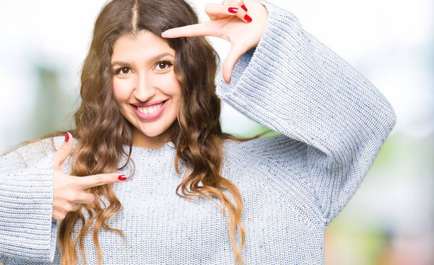 Mooie jongedame dragen winter trui glimlachend maken frame met handen en vingers met blij gezicht. Creativiteit en fotografie concept. - Foto, afbeelding