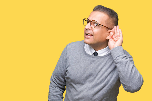 Homem árabe bussines meia idade vestindo óculos sobre fundo isolado sorrindo com a mão sobre orelha ouvindo uma audição para boatos ou fofocas. Conceito de surdez
. - Foto, Imagem