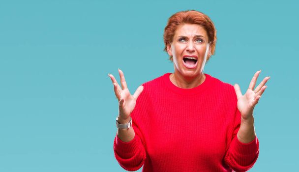 Atrractive senior caucasian redhead woman wearing winter sweater over isolated background crazy and mad shouting and yelling with aggressive expression and arms raised. Frustration concept. - Fotografie, Obrázek