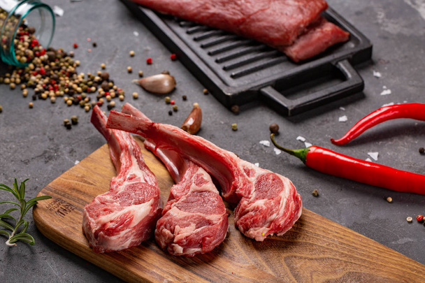 Set of Raw uncooked black angus beef tomahawk steaks on bones and veal tenderloin served with chilli and peppercorns. Rustic style. - Foto, Bild