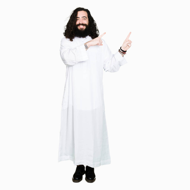 Мужчина в костюме Иисуса Христа улыбается и смотрит в камеру, указывая двумя руками и пальцами в сторону
. - Фото, изображение