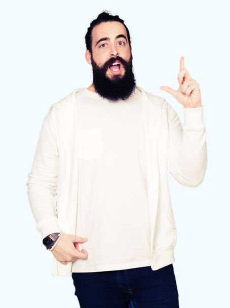 Молодий чоловік з довгим волоссям і бородою носить спортивний светр, вказуючи пальцем на успішну ідею. Вийшов і щасливий. Номер один
. - Фото, зображення