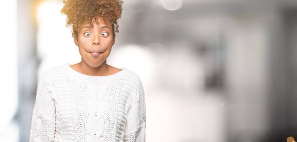 Beautiful young african american woman wearing winter sweater over isolated background making fish face with lips, crazy and comical gesture. Funny expression. - Foto, Bild