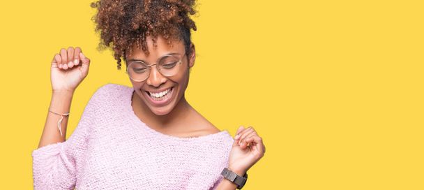 schöne junge afrikanisch-amerikanische Frau mit Brille über isoliertem Hintergrund tanzen fröhlich und fröhlich, lächelnd bewegt sich lässig und selbstbewusst Musik hören - Foto, Bild