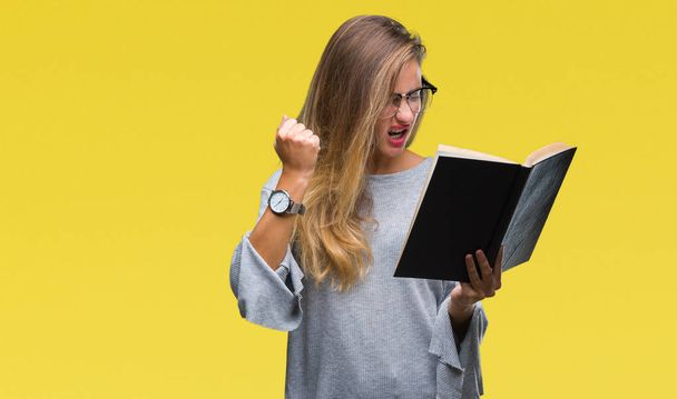 Jonge mooie blonde vrouw lezen van een boek over geïsoleerd background boos en gefrustreerd schreeuwen met woede, gek en schreeuwen met opgeheven hand, woede concept - Foto, afbeelding