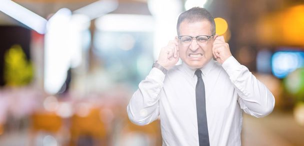 Homem árabe bussines meia idade vestindo óculos sobre fundo isolado cobrindo orelhas com dedos com expressão irritada para o ruído da música alta. Conceito de surdo
. - Foto, Imagem
