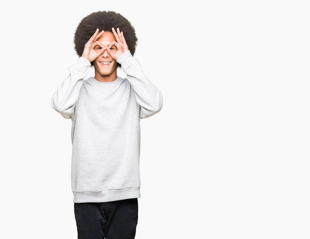Young african american man with afro hair wearing sporty sweatshirt doing ok gesture like binoculars sticking tongue out, eyes looking through fingers. Crazy expression. - Φωτογραφία, εικόνα