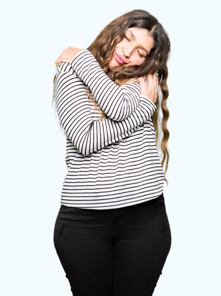 Young beautiful woman wearing stripes sweater Hugging oneself happy and positive, smiling confident. Self love and self care - Photo, Image