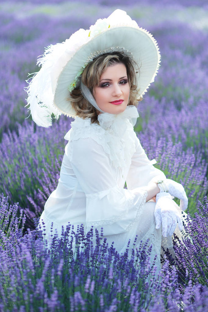 beautiful woman in victorian vintage style outfit and hat sitting on lavender field - Foto, afbeelding