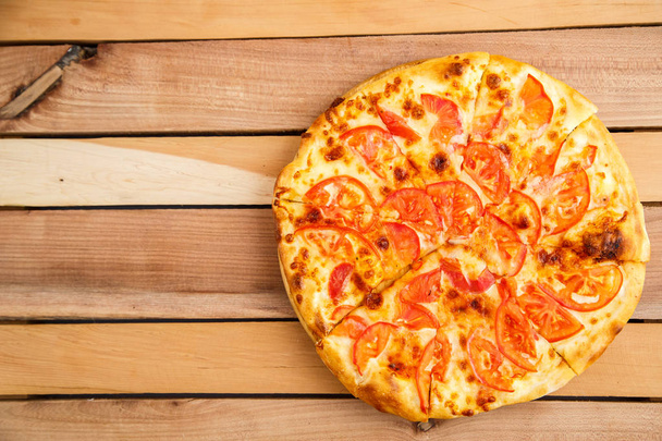 Pizza with tomatoes on a wooden tray on a wooden background. Top view - Photo, Image