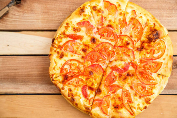 Pizza mit Tomaten auf einem hölzernen Tablett auf einem hölzernen Hintergrund. Ansicht von oben - Foto, Bild