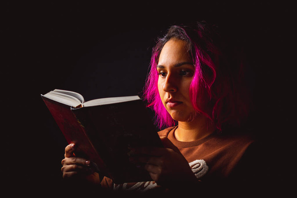 Portrait of young woman reading a book on black background low k - Photo, Image