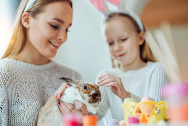 Look what a cute rabbit!The little daughter with her mother stroke a home decorative rabbit. - Fotoğraf, Görsel