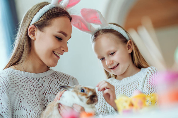 Easter fun!The little daughter with her mother stroke a home decorative rabbit. - Foto, imagen