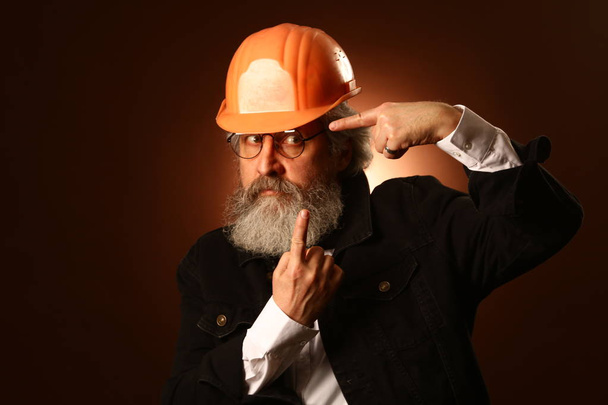 um trabalhador idoso em um capacete gestos sinais de alerta, retrato de estúdio
 - Foto, Imagem