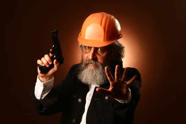 um trabalhador idoso em um capacete gestos sinais de alerta, retrato de estúdio
 - Foto, Imagem