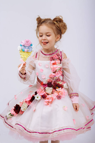 little girl in a pink dress with flowers holding a candy on a stick, licking, sweets in childhood. sweet life. - Foto, Imagen