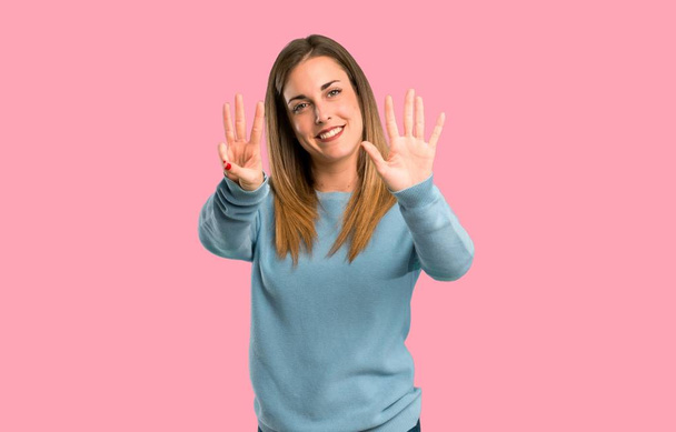 Blonde woman with blue shirt counting eight with fingers on isolated pink background - Photo, Image