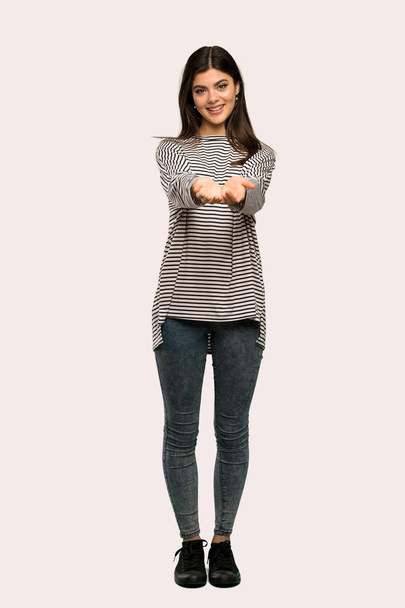 A full-length shot of a Teenager girl with striped shirt holding copyspace imaginary on the palm to insert an ad over isolated background - Fotó, kép