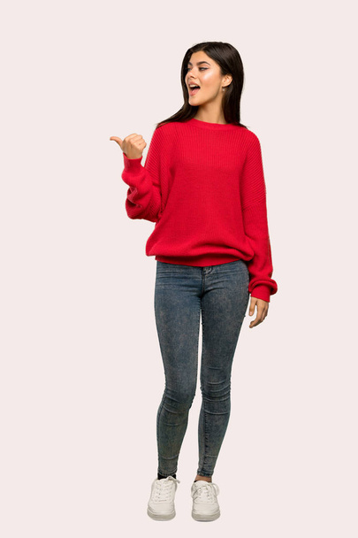 Uma foto completa de uma adolescente com camisola vermelha apontando para o lado para apresentar um produto sobre fundo isolado
 - Foto, Imagem
