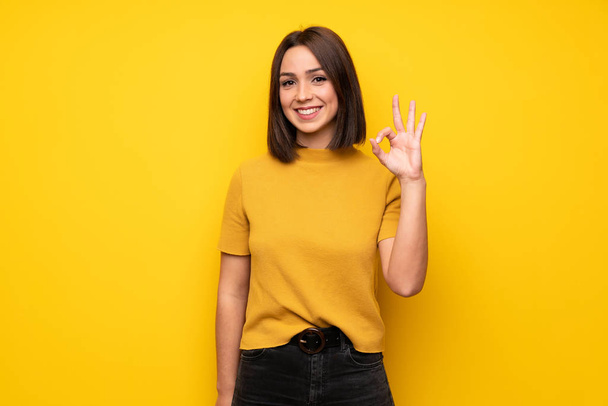 Jeune femme sur le mur jaune montrant ok signe avec les doigts
 - Photo, image