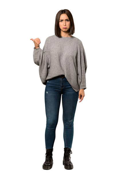 A full-length shot of a Young woman unhappy and pointing to the side over isolated white background - Foto, Bild