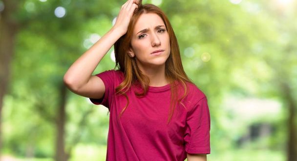 Young redhead girl with an expression of frustration and not understanding in the park - 写真・画像