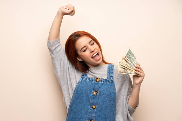 Jonge roodharige vrouw over geïsoleerde achtergrond nemen een heleboel geld - Foto, afbeelding