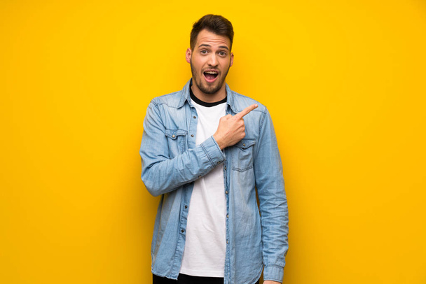 Handsome man over yellow wall surprised and pointing side - Foto, Imagem