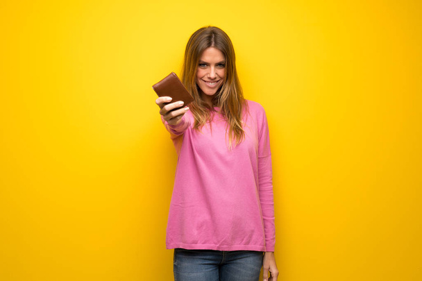 Vrouw met roze trui over gele muur houdt een portefeuille - Foto, afbeelding