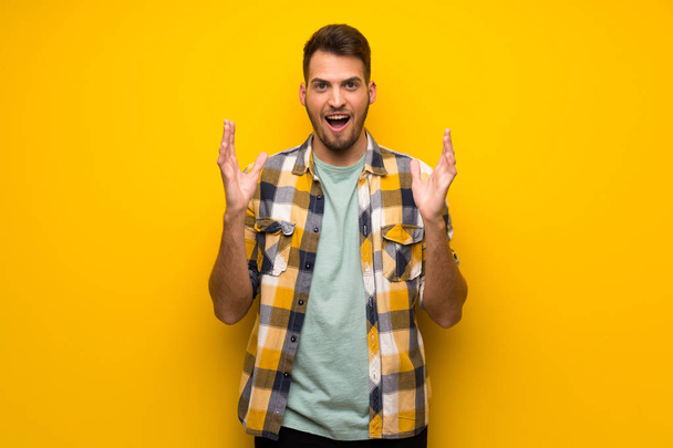 Hombre guapo sobre pared amarilla con expresión facial impactada
 - Foto, imagen