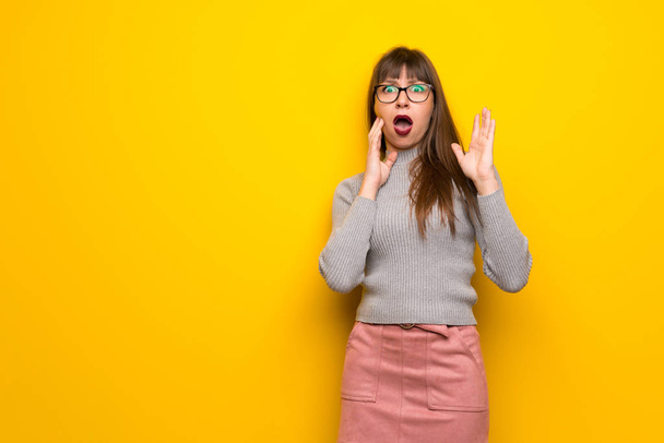 Женщина в очках на желтой стене удивлена и шокирована, глядя направо
 - Фото, изображение
