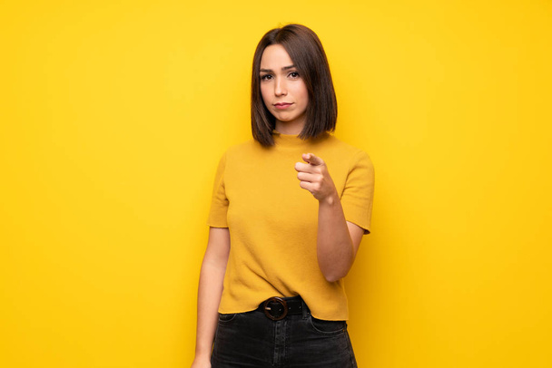 Young woman over yellow wall frustrated and pointing to the front - Фото, изображение