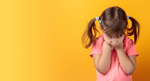 Offended girl in a pink t-shirt on an orange background. - Photo, image