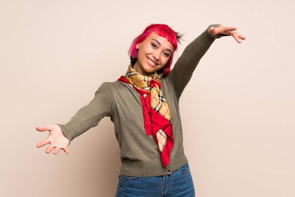 Young woman with pink hair over yellow wall presenting and inviting to come with hand - Foto, afbeelding