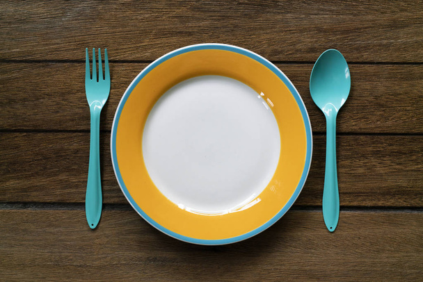 Empty color plate, fork and spoon on wooden table background, to - Photo, image