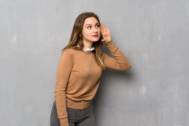 Девочка-подросток над текстурированной стеной слушает что-то, прикладывая руку к уху
 - Фото, изображение