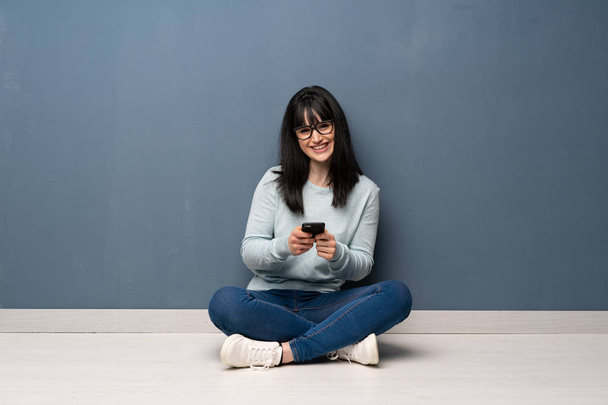 Femme assise sur le sol envoyant un message avec le mobile
 - Photo, image