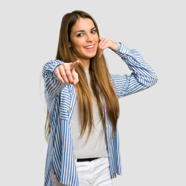 Jeune fille avec chemise rayée faisant geste de téléphone et pointant devant sur fond gris isolé
 - Photo, image