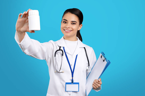 Photo of pretty charming young woman doctor holding bottle of pills and clipboard over blue background. - Foto, Bild