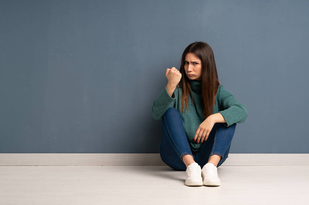 Young woman sitting on the floor with angry gesture - Foto, imagen