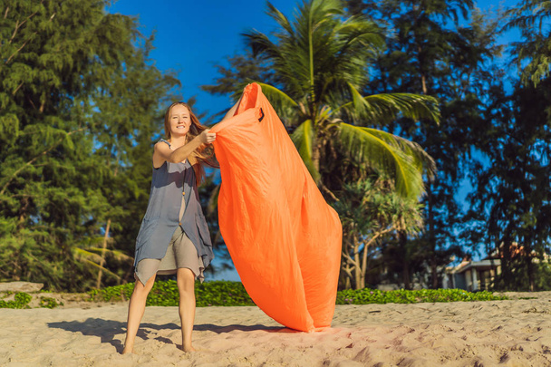 Summer lifestyle portrait of woman inflates an inflatable orange sofa on the beach of tropical island. Relaxing and enjoying life on air bed - Foto, Imagen