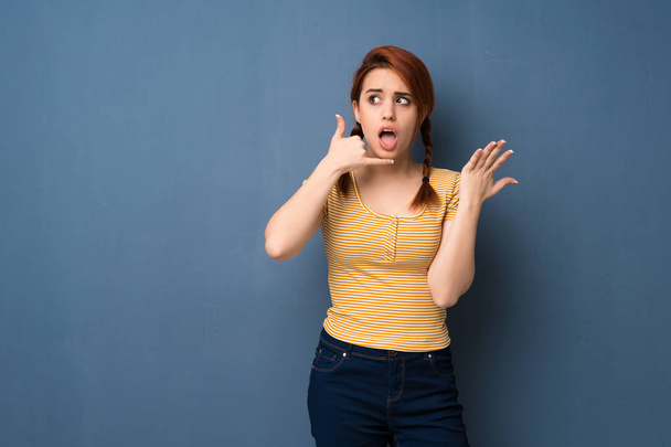 Nuori punapää nainen yli sininen tausta tehdä puhelimen ele ja epäillä
 - Valokuva, kuva