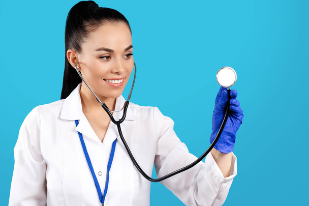 Portrait de jeune femme brillante médecin utilisant stéthoscope sur fond bleu
. - Photo, image