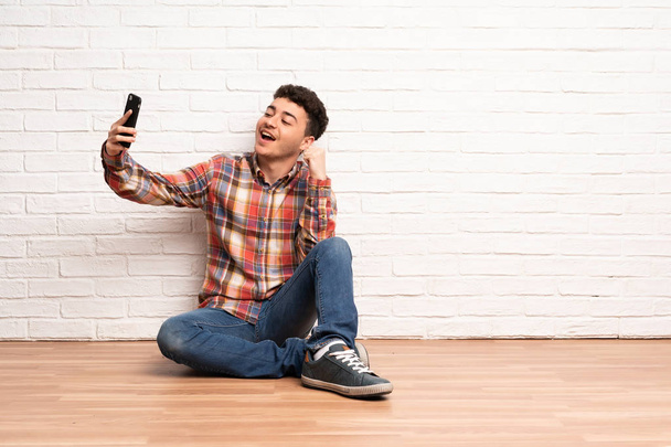 Young man sitting on the floor making a selfie - Fotoğraf, Görsel