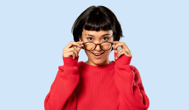 Short hair girl with red sweater with glasses and surprised on isolated blue background - Photo, Image