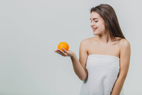 Retrato de una linda joven atractiva mujer de medio ojo sosteniendo una naranja en sus manos y mirando a una naranja, aislada sobre un fondo blanco
. - Foto, imagen