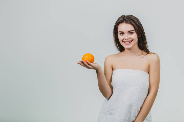 Portrait of a cute young attractive half-woman holding an orange orange on her hands and looking at the camera, isolated over a white background. - Foto, Bild